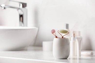 Photo of Holder with natural face rollers on counter in bathroom. Space for text