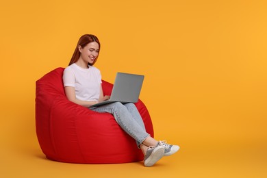 Photo of Smiling young woman working with laptop on beanbag chair against yellow background, space for text