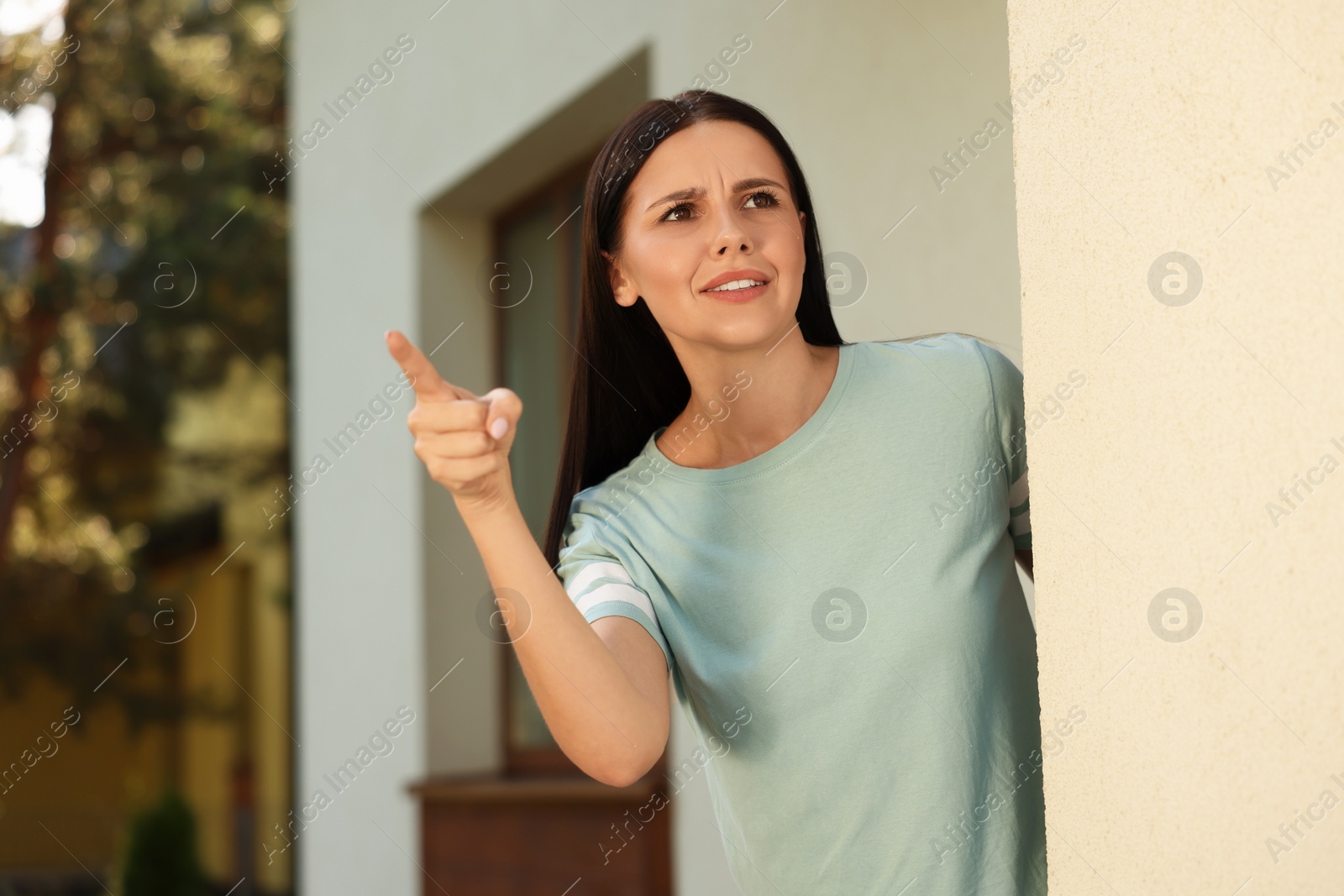 Photo of Angry young woman pointing near house. Annoying neighbour