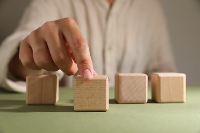 Photo of Woman choosing wooden cube among others at green table, closeup