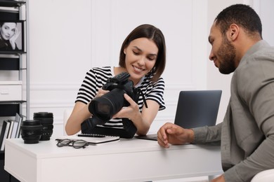 Young professional photographer showing camera to man in modern photo studio