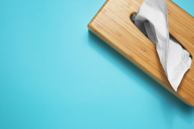 Photo of Wooden holder with paper tissues on light blue background, top view. Space for text