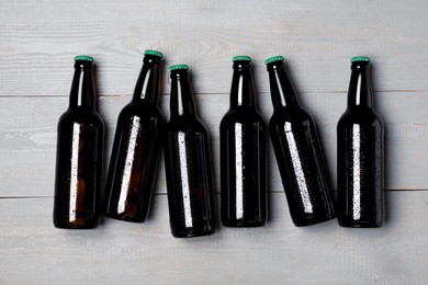 Photo of Glass bottles of beer on grey wooden background, flat lay