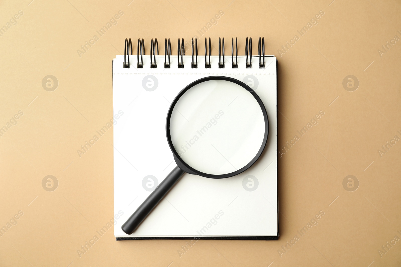 Photo of Magnifier glass and empty notebook on beige background, flat lay with space for text. Find keywords concept