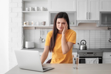 Photo of Young woman suffering from headache in kitchen