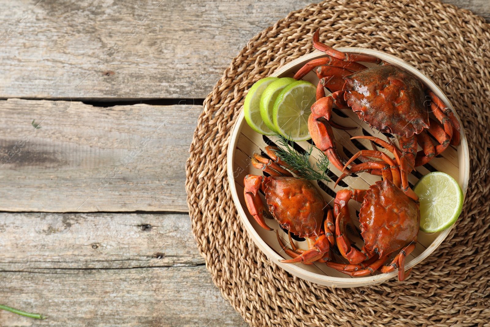 Photo of Delicious boiled crabs with lime and dill in bamboo steamer on wooden table, top view. Space for text