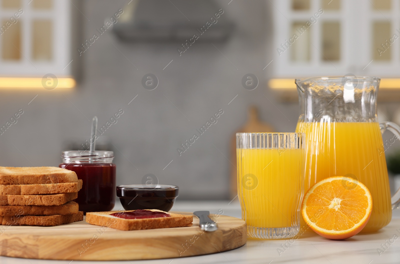 Photo of Breakfast served in kitchen. Crunchy toasts, jam and orange fresh on white table