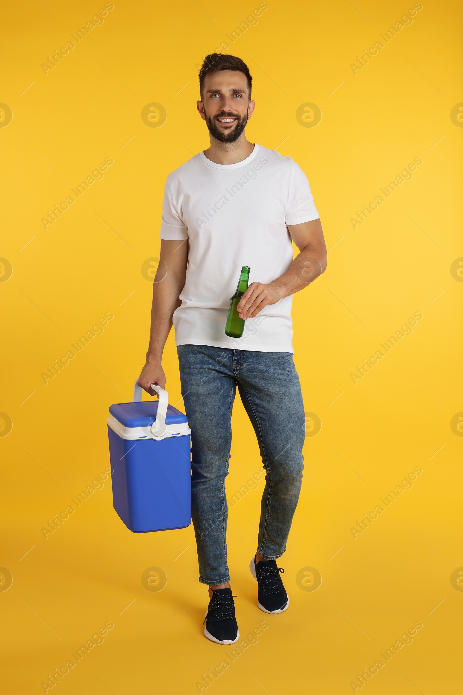 Photo of Happy man with cool box and bottle of beer on yellow background