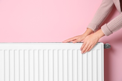Photo of Woman warming hands on heating radiator near color wall