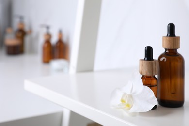 Photo of Bottles of essential oil and orchid flower on white shelf in bathroom. Space for text