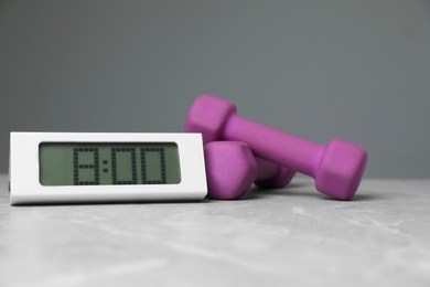 Alarm clock and dumbbells on table against grey background. Morning exercise