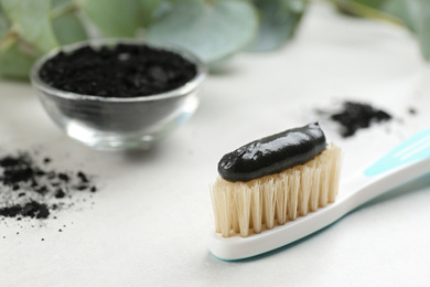 Photo of Toothbrush with natural bristles and charcoal paste on white table, closeup. Space for text