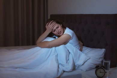 Photo of Young woman with terrible headache sitting in bed at night