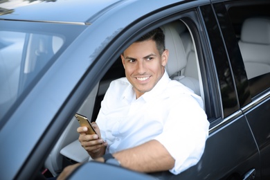 Photo of Handsome man using smartphone in modern car