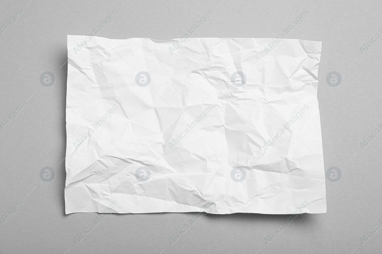 Photo of Sheet of white crumpled paper on grey background, top view