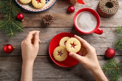 Woman eating traditional Christmas Linzer cookies with sweet jam at table, top view