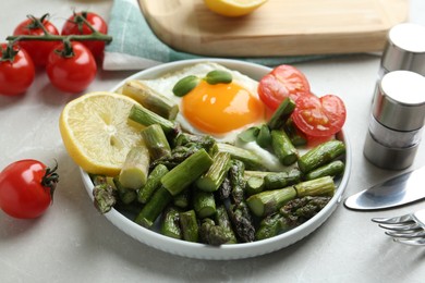 Oven baked asparagus served with fried egg on light grey marble table