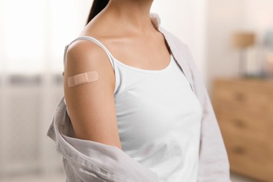 Photo of Woman with sticking plaster on arm after vaccination at home, closeup