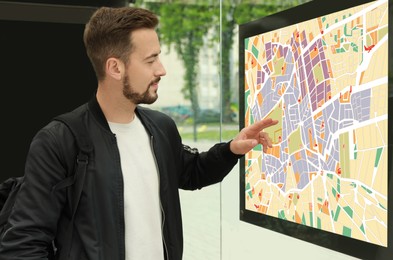 Image of Young man with backpack near public transport map at bus stop