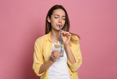 Photo of Young woman drinking lemon water on pink background