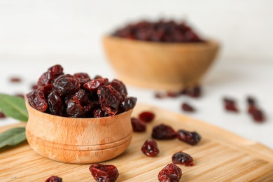 Tasty dried cranberries in bowl on wooden board. Space for text