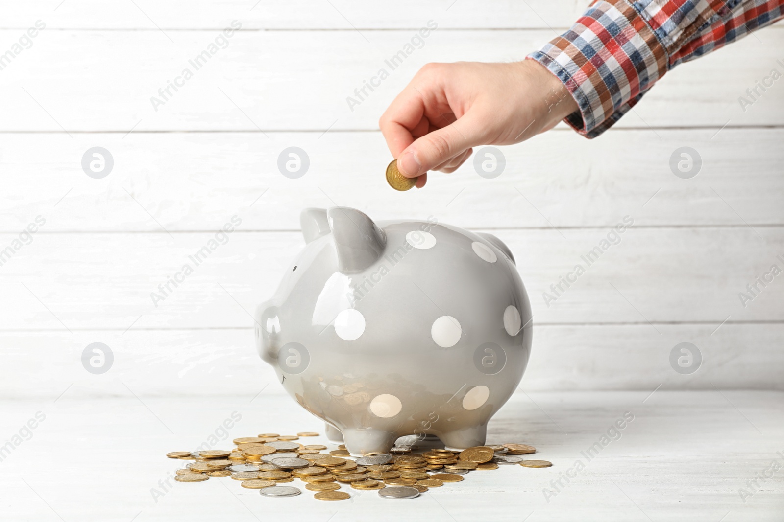 Photo of Man putting coin into piggy bank on table