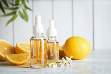 Photo of Bottles of citrus essential oil, flower and lemons on white wooden table. Space for text