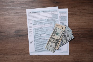 Photo of Payroll. Tax return forms and dollar banknotes on wooden table, flat lay