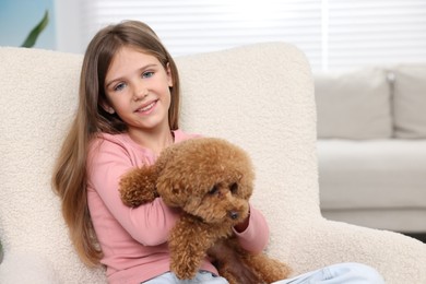Photo of Little child with cute puppy in armchair at home, space for text. Lovely pet