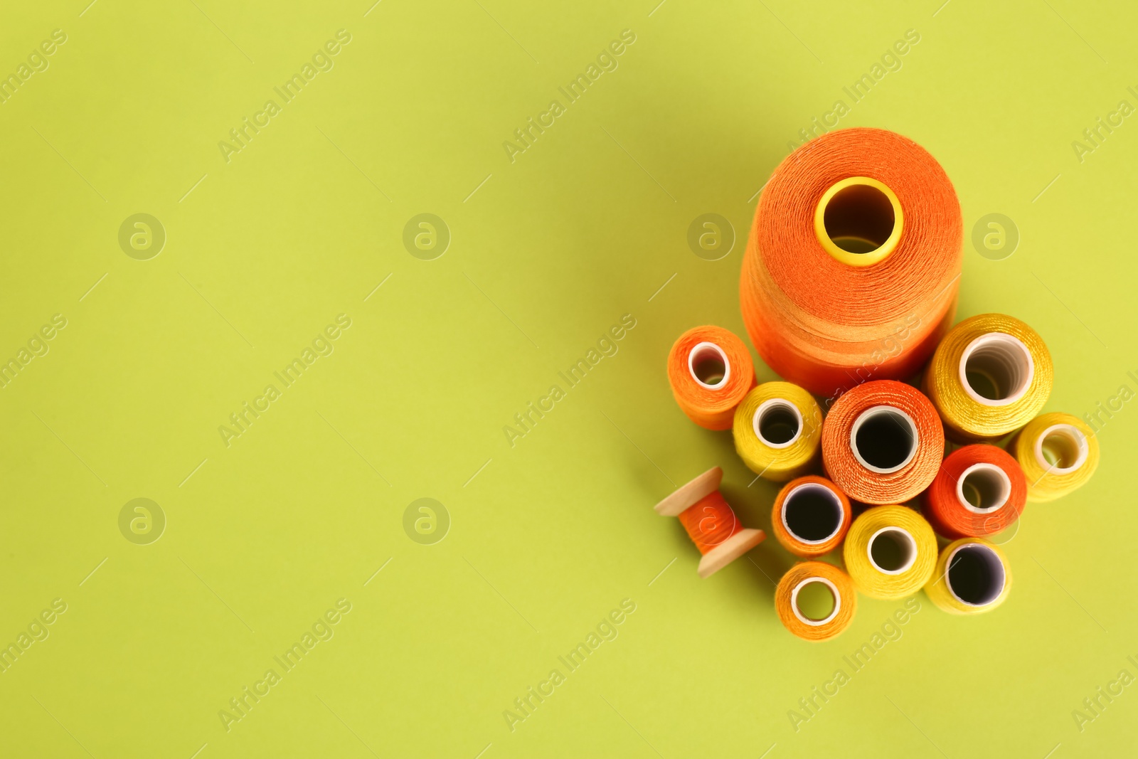 Photo of Different shades of orange and yellow sewing threads on light green background, flat lay. Space for text