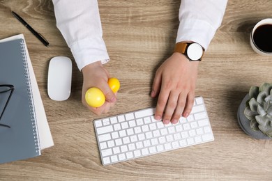 Photo of Man squeezing yellow stress ball while typing on computer keyboard at table, top view