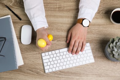 Man squeezing yellow stress ball while typing on computer keyboard at table, top view