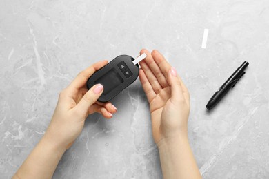 Photo of Diabetes. Woman checking blood sugar level with glucometer at gray marble table, top view