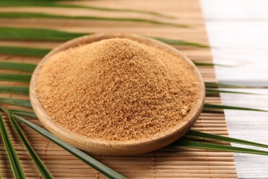 Photo of Coconut sugar, palm leaves and bamboo mat on wooden rustic table, closeup