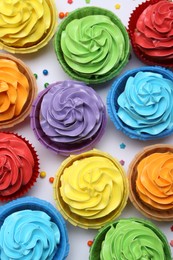 Photo of Many tasty cupcakes with bright cream and sprinkles on white background, flat lay