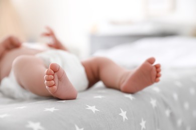 Cute little baby in diaper lying on bed in room, closeup