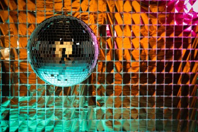 Photo of Shiny disco ball against foil party curtain under turquoise and orange light, space for text