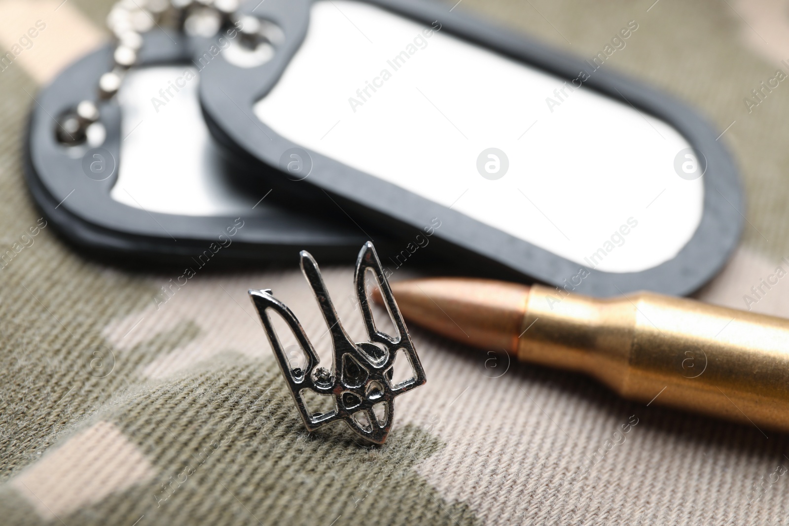 Photo of Ukrainian trident near military ID tags and bullet on camouflage background, closeup