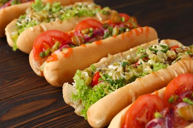 Photo of Different tasty hot dogs on wooden table, closeup