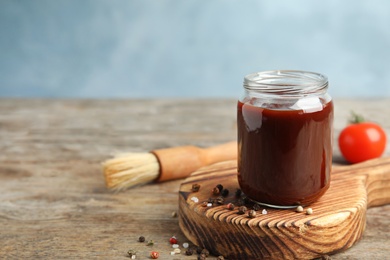 Photo of Composition with jar of barbecue sauce on wooden table. Space for text