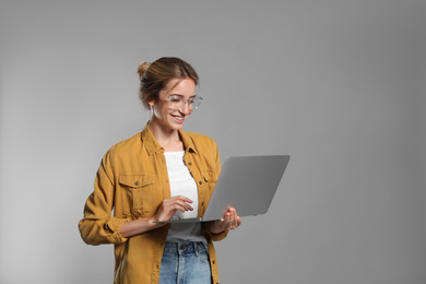 Portrait of young woman with modern laptop on grey background