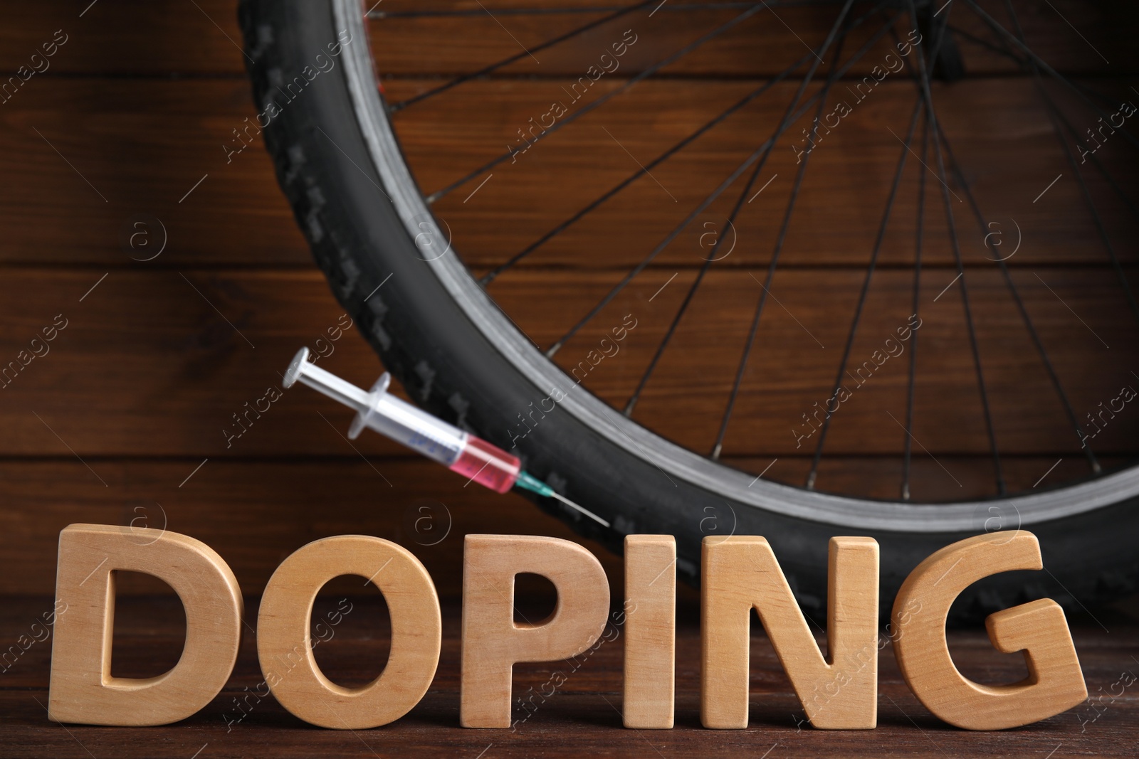 Photo of Word Doping, syringe and bicycle wheel on wooden background