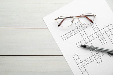 Crossword with answers, glasses and pen on white wooden table, top view. Space for text