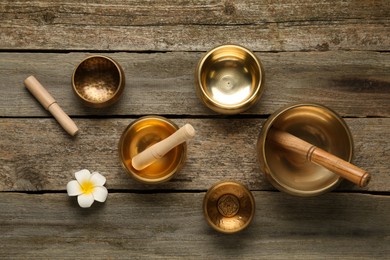 Golden singing bowls, mallets and flower on wooden table, flat lay