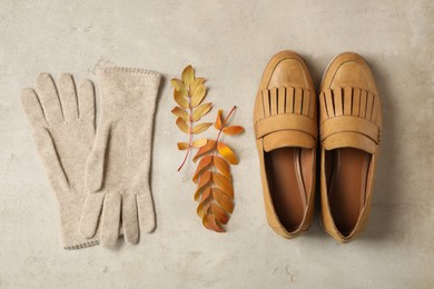 Photo of Stylish woolen gloves, pair of shoes and dry leaves on beige table, flat lay