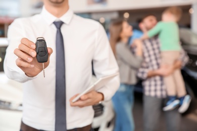 Photo of Salesman with key and young family in car salon