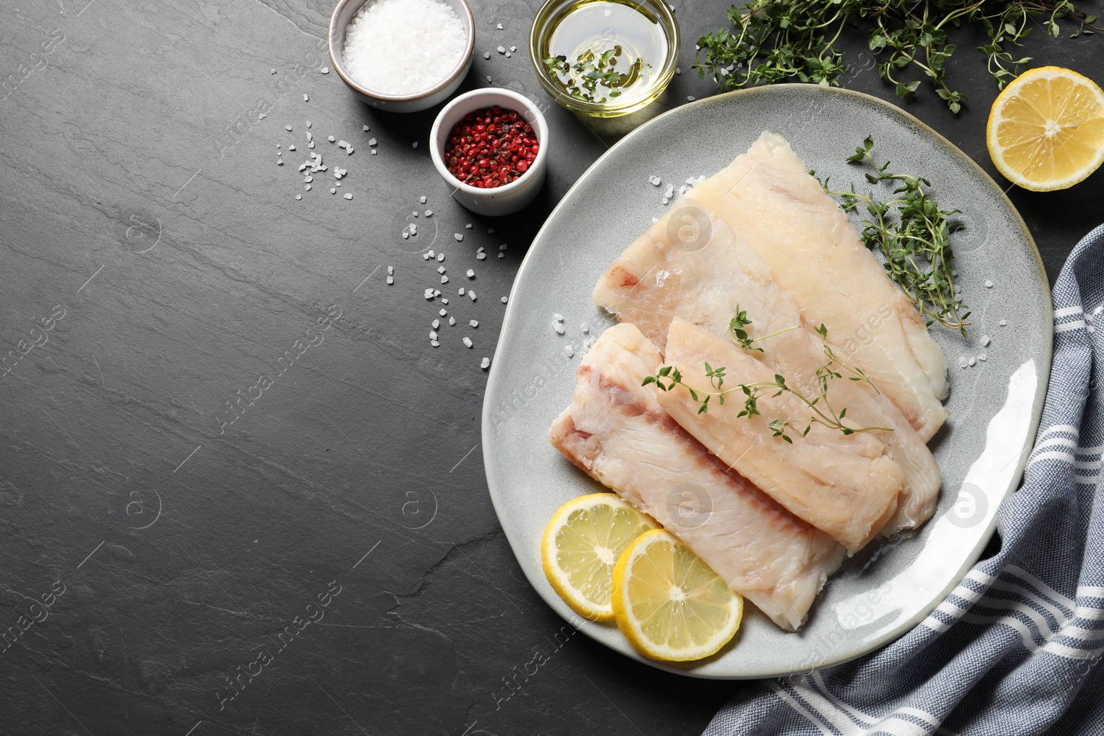 Photo of Plate with raw cod fish, microgreens, spices and lemon on dark textured table, flat lay. Space for text