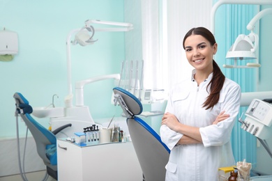 Young female dentist in white coat at workplace. Space for text