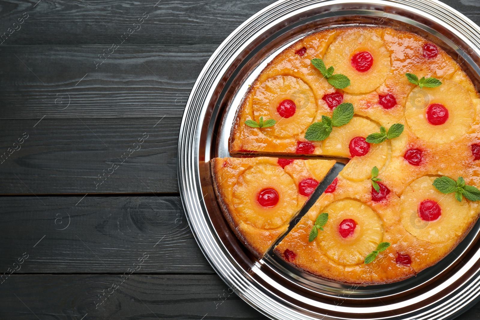 Photo of Delicious cut pineapple pie with cherry and mint on black wooden table, top view. Space for text