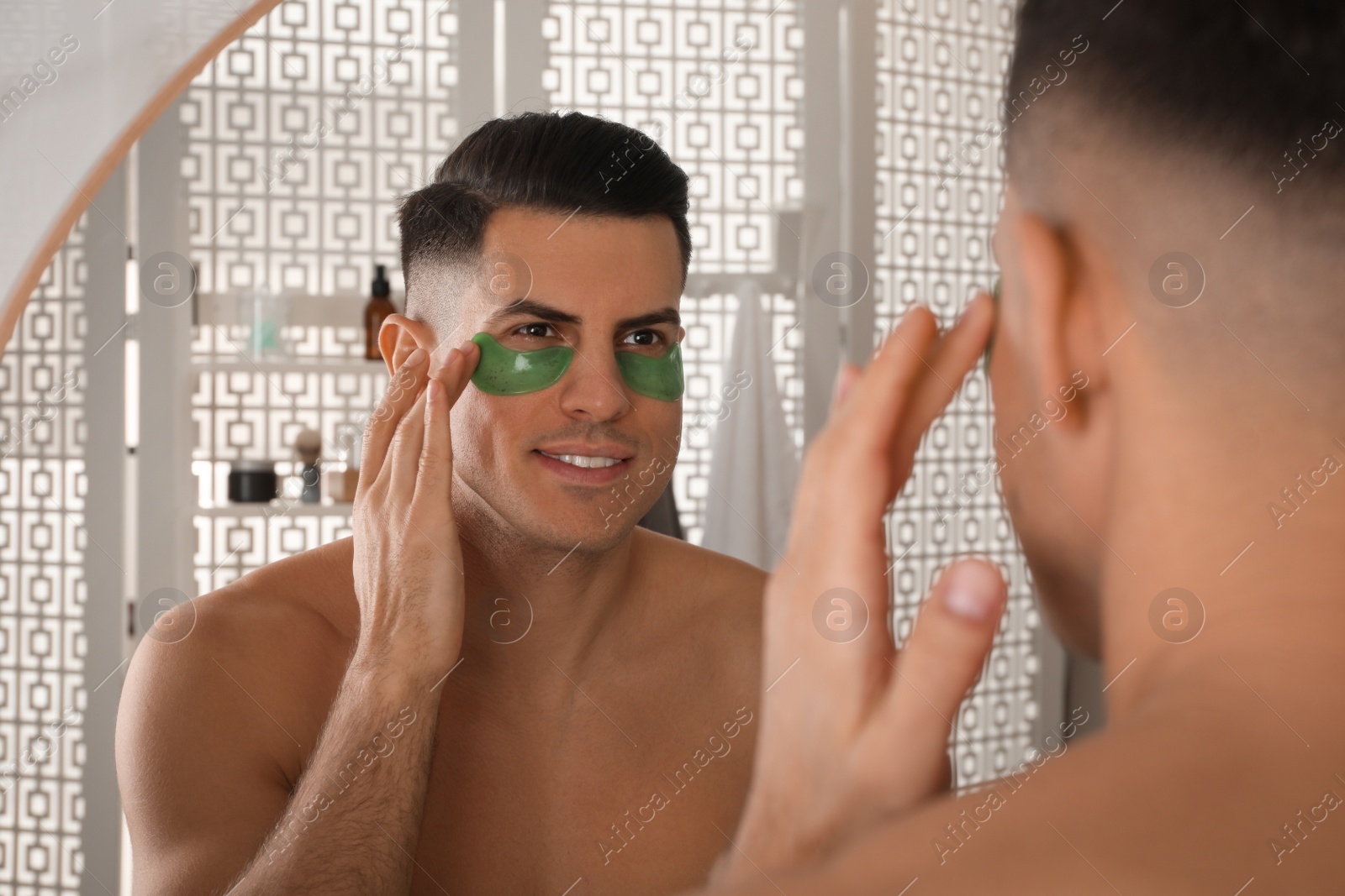 Photo of Man applying green under eye patch near mirror at home